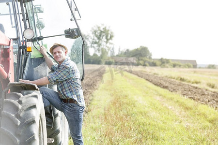 自信的农民攀登拖拉机的肖像在农场