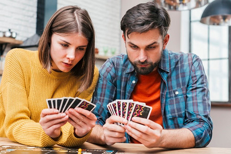 严肃的年轻夫妇看他们的牌玩棋盘游戏