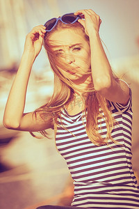 夏季时尚。肖像女孩在蓝色心形太阳镜享受夏天微风在日落在码头