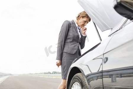 担心的女商人看着故障汽车在道路上反对天空