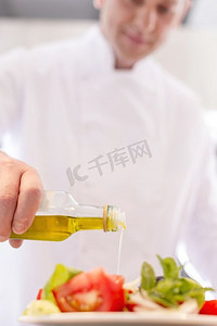 成熟的厨师使用浇油沙拉在盘子在餐厅