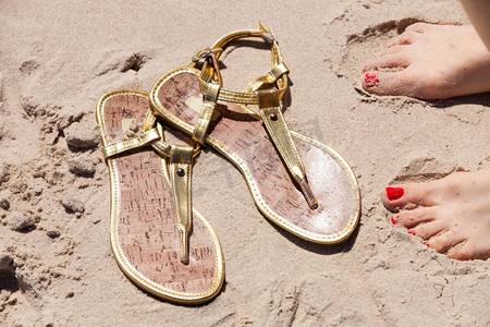 女人脚与红色画指甲旁边优雅的人字拖在沙滩上，沙滩鞋夏天的时间。女人脚旁边的人字拖