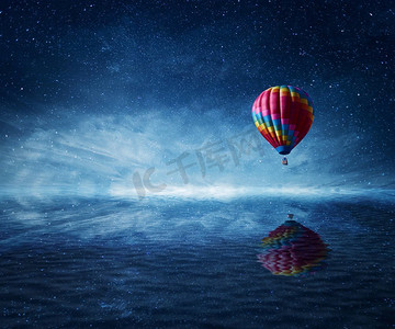 深蓝色星空背景摄影照片_热气球飞过冰冷的深蓝色海面。奇妙的风景与星空背景和水反射。