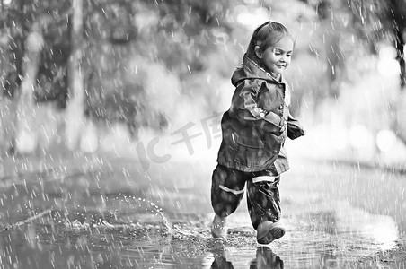 雨中儿童摄影照片_快乐的小女孩在雨中的水坑里走着、跳着