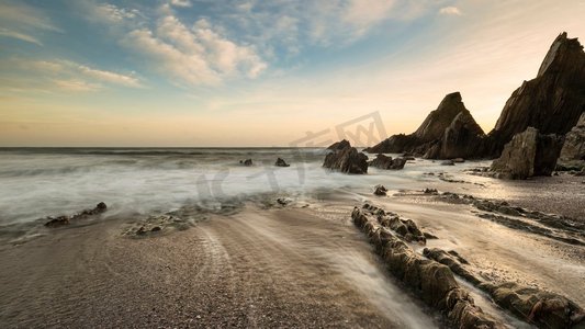 Westcombe海滩美丽的日落风景图象在德文郡英格兰与锯齿状岩石在海滩和惊人的云形成