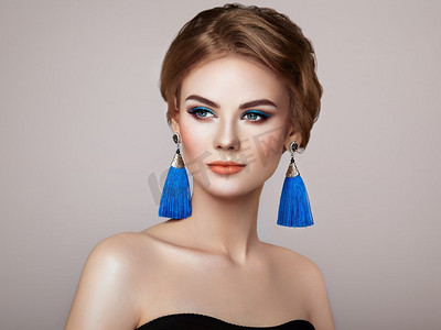 美丽的女人与大耳环流苏珠宝蓝色颜色。完美的化妆和优雅的发型。蓝色化妆箭头