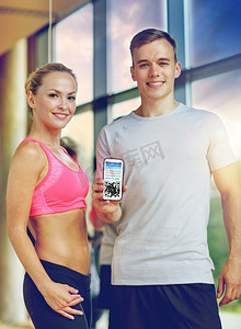 疫情码摄影照片_健身，运动和疫苗接种概念—快乐的夫妇与二维码智能手机在健身房。快乐的夫妇与QR码在智能手机在健身房