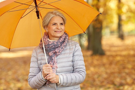 老年、天气和季节概念秋季公园打伞快乐老妇人写真。秋天公园里打伞的快乐老妇人