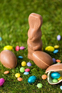 bonbon摄影照片_复活节，糖果和糖果概念—关闭巧克力兔子，鸡蛋和糖果滴在草。巧克力兔子，鸡蛋和糖果滴在草地上