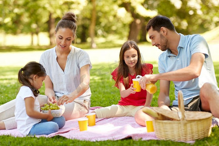 吃葡萄摄影照片_家庭，休闲和人的概念—快乐的母亲，父亲和两个女儿在夏季公园野餐。快乐的家庭有野餐在夏天公园