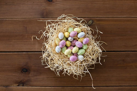 bonbon摄影照片_复活节，糖果和假日概念—糖果下降蛋在稻草巢在木背景复活节彩蛋在稻草巢在木桌