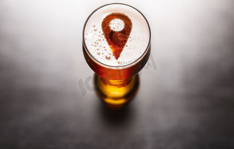 本地啤酒的概念。位置别针标志在黑色桌子上的啤酒泡沫玻璃上，从上面看。本土啤酒概念