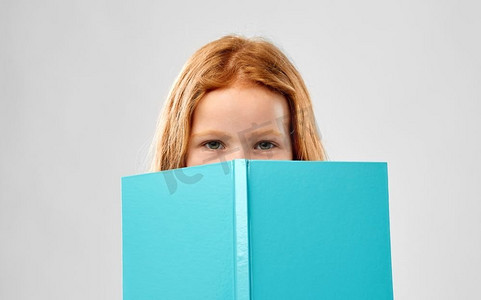童年和人的概念—微笑的红头发女孩读书在灰色背景的书。微笑的红色头发的女孩读书