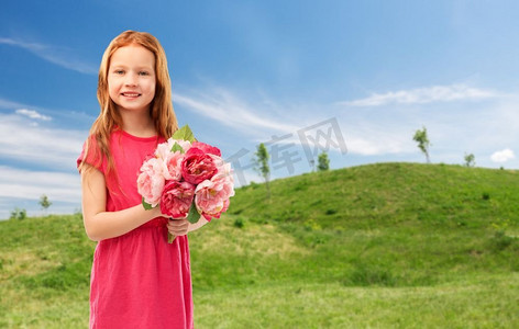 童年和人概念—快乐的红头发女孩有花在蓝天和绿色草甸背景快乐的红色头发的女孩与花