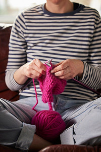 关闭的妇女坐在沙发上在家编织跳线与粉红色羊毛