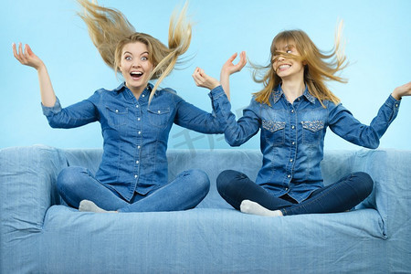 两个滑稽震惊的女人穿着风吹金发的牛仔裤衬衫。蓝色背景..两个头发被风吹得心惊肉跳的幸福女人