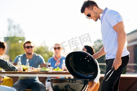 休闲与人的概念-快乐的男人在屋顶派对上烧烤烧烤和朋友。男人在屋顶派对上烧烤