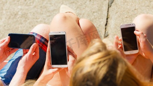 浏览互联网摄影照片_朋友在户外使用手机发短信。妇女和男子在智能手机上浏览互联网。夏天放松朋友的男人和女人使用手机。