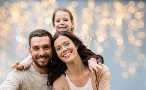 节日灯光摄影照片_家庭和人民概念—快乐的母亲，父亲和小女儿在节日灯光背景。在节日灯光背景的快乐家庭