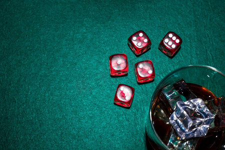扑克桌桌摄影照片_红色骰子威士忌玻璃杯配冰块扑克桌