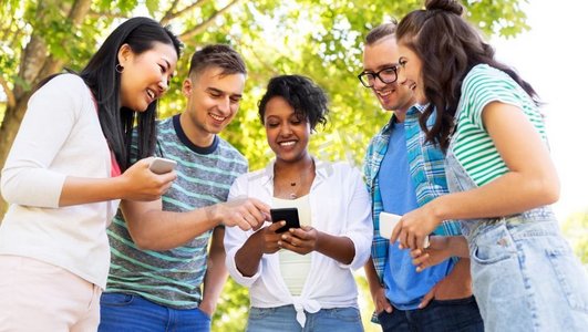 友谊，技术和国际概念—一群朋友在夏季公园与智能手机。快乐的朋友与智能手机在夏季公园