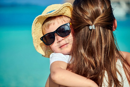 三岁的蹒跚学步的男孩在海滩上给他的母亲一个拥抱。暑假在马尔代夫度假。