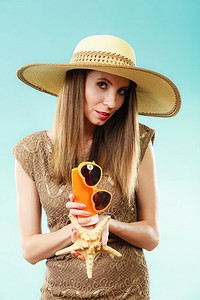 假日夏日时尚护肤理念。戴草帽的女子手持太阳镜外壳和防晒霜，蓝色背景