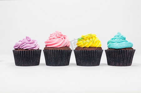 淡绿色蓝色摄影照片_四个巧克力杯蛋糕糖霜或糖霜，粉红色，紫色，蓝色和黄色与绿叶，拍摄在白色背景