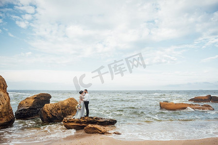 同一对夫妇带着一位穿着蓝色连衣裙的新娘走在海边