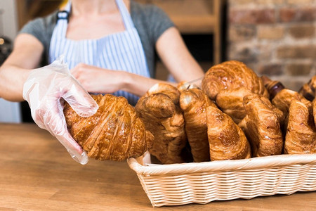 女面包师戴着塑料手套的手从篮子里拿烤羊角面包