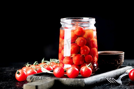 泡菜腌制摄影照片_把腌制的西红柿放在切菜板上的玻璃瓶里。在黑色背景上。高质量的照片。把腌制的西红柿放在切菜板上的玻璃瓶里。