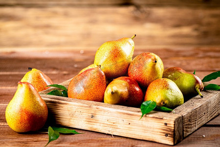 新鲜的梨子放在有叶子的托盘上。背景是木制的。高质量的照片。新鲜的梨子放在有叶子的托盘上。