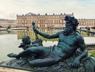 公园与建筑摄影照片_法国巴黎附近凡尔赛宫花园中的青铜雕塑与喷泉水中的倒影。