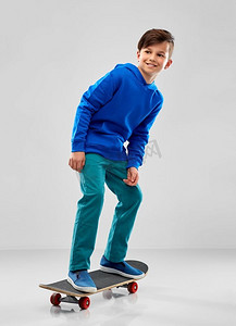 童年，休闲和人的概念-微笑的男孩穿着蓝色连帽衫，灰色背景上有滑板。微笑的男孩，穿着蓝色连帽衫，带着滑板