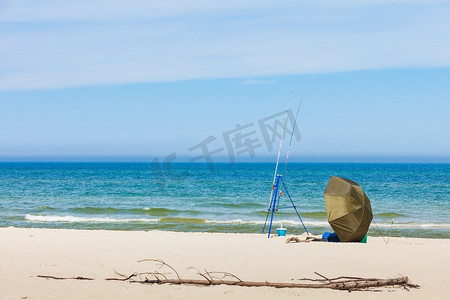 夏季帐篷摄影照片_钓鱼竿和帐篷独自留在海滩海岸。阳光明媚的夏季天气海边钓鱼竿和帐篷