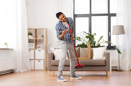 清洁、家务和家政概念-印度男人扫地，在家唱歌。一个男人在家里打扫扫帚，唱歌