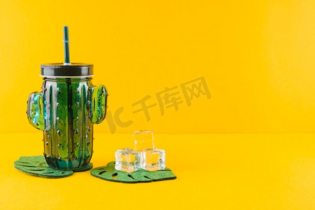 建筑冰块摄影照片_玻璃仙人掌汁罐水晶冰块叶杯垫反对黄色背景