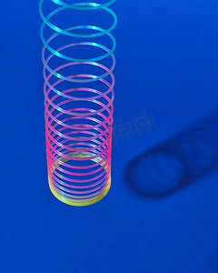 在蓝色背景与阴影之上的拉伸彩虹塑料弹性玩具，文本的地方经典的彩色塑料弹簧挂钩与阴影。