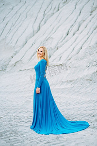 金发女郎在一件蓝色连衣裙与蓝色眼睛在一个花岗岩采石场反对砾石的背景