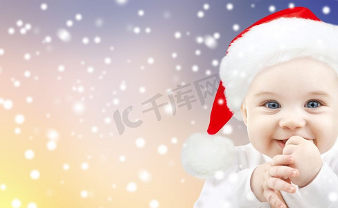 圣诞节，节日和人们的概念-戴着圣诞帽的小男婴在雪的背景下。圣诞节戴着圣诞帽的小男婴