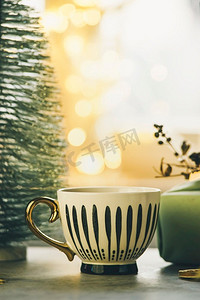 空的条纹杯在桌子上与小圣诞树和金色散景灯。舒适的冬天在家里。前视图。