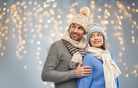圣诞围巾摄影照片_人和冬季假期概念—在编织的帽子和围巾的愉快的夫妇在圣诞节光背景快乐的夫妇在冬天的衣服