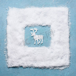 雪摄影照片_创意圣诞节概念与白色鹿在淡蓝色背景，顶视图的雪框架节日贺卡。寒假概念