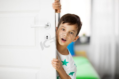 童年，情感和人的概念—惊讶的小男孩在家里的门后。在家里的门后惊讶的小男孩