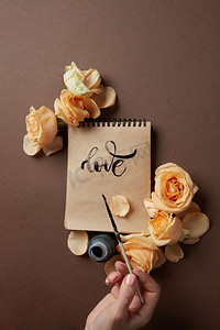 手写浪漫情书摄影照片_女孩写了一个祝贺爱的棕色背景与玫瑰。手用画笔写情书