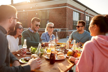 休闲与人际概念—快乐的朋友在天台享用晚餐或烧烤派对。快乐的朋友与饮料或烧烤党在屋顶