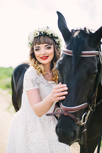 女孩红色的嘴唇在白色的裙子附近的一匹黑马