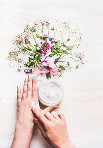 女性手应用奶油在皮肤在白色背景与植物和花，顶视图.天然化妆品概念
