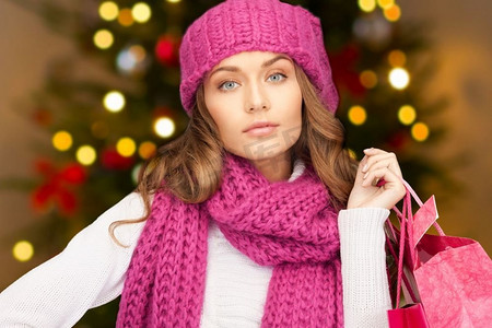 冬天购物袋摄影照片_人，节日和销售概念--圣诞树上的购物袋女人的背景。拿着购物袋的女人挂着圣诞彩灯