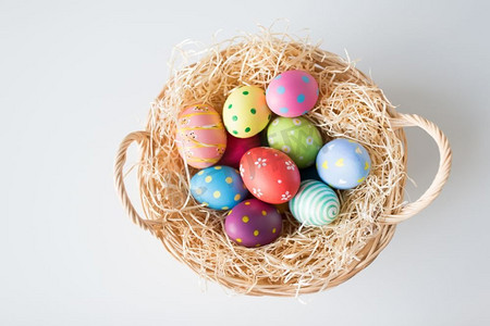 传统画摄影照片_复活节，假日和传统概念—在篮子的彩色鸡蛋有稻草在白色背景彩色复活节彩蛋